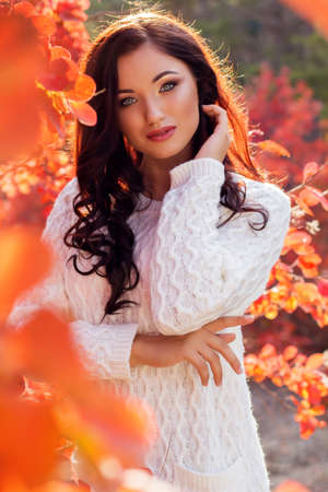 Portrait of beautiful pretty girl with fashion makeup and flawness skin is wearing white warm sweater in autumn parkの写真素材