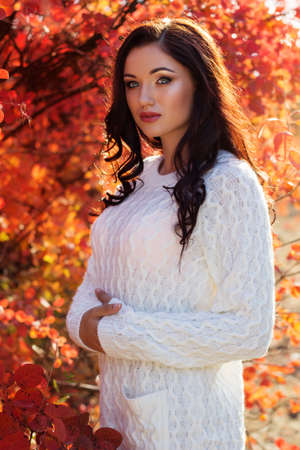 Portrait of beautiful pretty smiling girl with fashion makeup and flawness skin is wearing white warm sweater in autumn colorful parkの写真素材