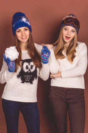 Two pretty teenager girls in winter clothes over brown background, winter conceptの写真素材