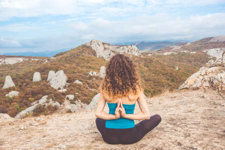 Young curly girl doing yoga meditation in beautiful mountains landscapeの写真素材