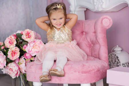 Pretty happy child girl is wearing fashion dress sitting on chair near rose flowers, birthday conceptの写真素材