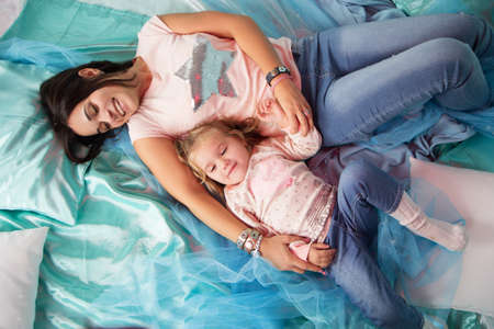 Mother and little girl having time together in blue bedの写真素材