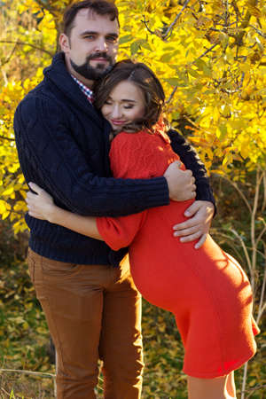 Happy future parents wife and husband are wearing warm clothes spending time in autumn park with...