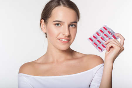 Portrait of young caucasian girl with perfect skin and nude makeup isolated on white in studio is holding medicaments in handsの写真素材