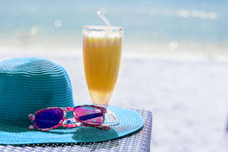 Orange fresh juice, hat and sunglasses near seaの写真素材