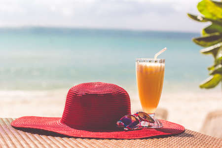 Orange fresh juice, hat and sunglasses over seaの写真素材