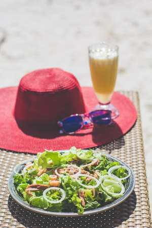 Seafood salad, orange fresh juice, hat and sunglasses on the table near seaの写真素材
