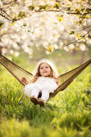 Pretty child girl is sitting in hammock outdoorsの写真素材