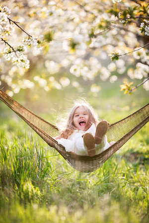 Happy child girl in hammock in blossom gardenの写真素材