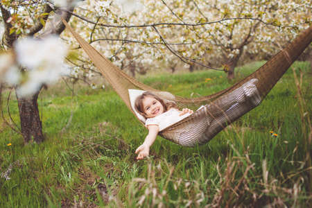 Happy child girl is resting in hammock in gardenの写真素材