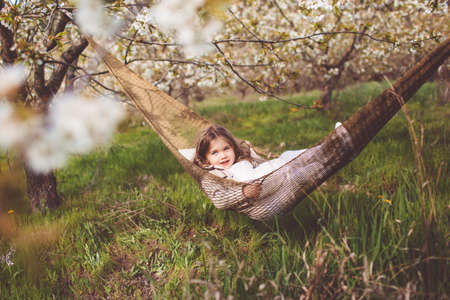 Child girl is resting in hammock in cherry gardenの写真素材