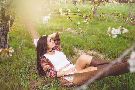 Woman is reading book in hammock in gardenの写真素材