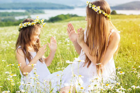 Cute child girls is playing at  green camomile field with mountains viewの写真素材