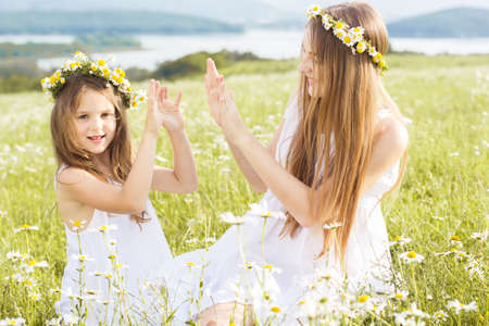 Cute child girls is playing at  green camomile field with mountains viewの写真素材
