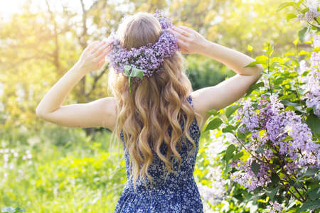 Girl with wreath from lilac purple flowers in green park, spring timeの写真素材