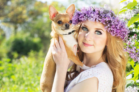 Beautiful blonde teen girl with a wreath of lilac flowers and small chuhuahua dogの写真素材