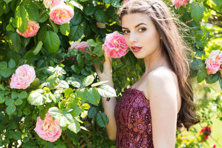Beautiful young woman with fashion makeup posing near pink roses in a gardenの写真素材