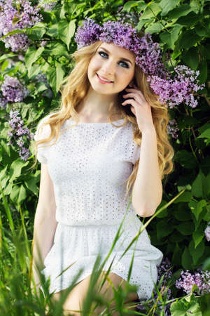 Beautiful blonde girl is wearing wreath of lilac flowers, summer timeの写真素材