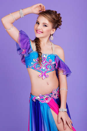 Beautiful belly dancer child girl is wearing a colorful fashion costume. Isolated on purpleの写真素材