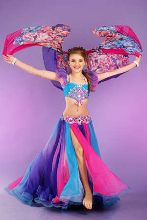 Beautiful belly dancer girl is wearing a colorful fashion costume. Isolated on purpleの写真素材