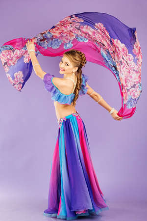 Beautiful belly dancer girl is wearing a colorful fashion costume. Isolated on purpleの写真素材