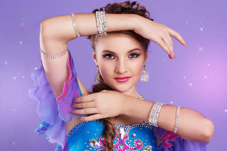 Portrait of beautiful belly dancer girl with nice makeup and heardress is wearing a colorful fashion costume. Isolated on purpleの写真素材