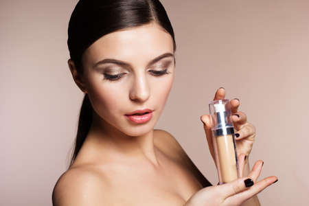 Portrait of a naturally beautiful woman is holding foundation tube that makes skin flawless and perfectの写真素材
