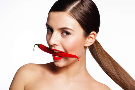 Portrait of beautiful brunette girl is holding hot red cayennes in her teethの写真素材