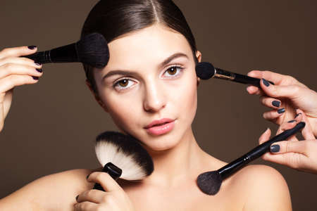 Portrait of a naturally beautiful woman with perfect skin is holding brushes for makeupの写真素材