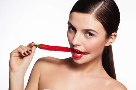 Portrait of beautiful brunette girl is holding hot red cayennes in her mouthの写真素材