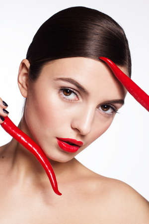 Portrait of beautiful brunette girl with pefrect skin is holding hot red cayennesの写真素材