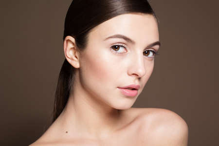 Portrait of a naturally beautiful girl with flawless perfect skin isolated on brownの写真素材