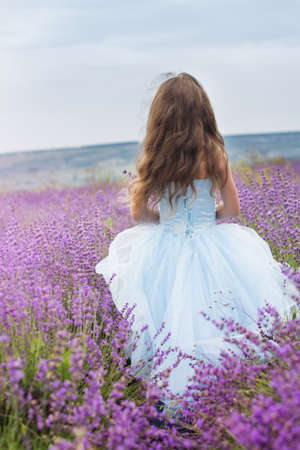 happy little girl is in a lavender field holds a basket with ribbonの写真素材
