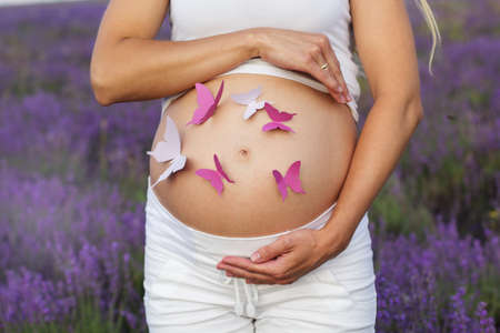 Beautiful pregnant blonde woman with butterflies on her stomach resting in the lavender field