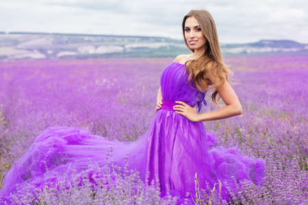 Beautiful sexy woman is wearing magic purple fashion dress posing at field of purple lavender flowersの写真素材