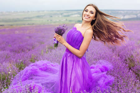 Beautiful sexy woman is wearing princess purple fashion dress posing at field of purple lavender flowersの写真素材