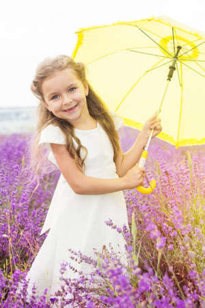 Happy little girl is in a lavender field holds an yellow umbrellaの写真素材