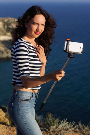 Tourist smiling slim girl making selfie picture with stick on the peak of mountain over sea...