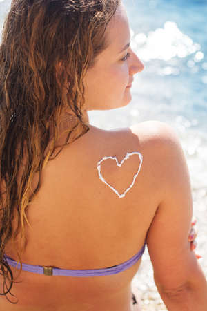 Sunscreen tan lotion heart shape drawing on woman backの写真素材