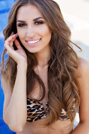 Sexy smiling woman is wearing leopard printed bikini with tanned skin is sitting near swimming pool on sunbed, summer timeの写真素材