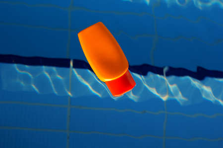 Orange jar with sunscreen cream is swimming in swimming pool with blue water, summer timeの写真素材