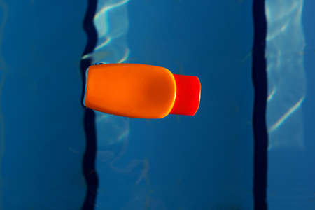 Orange jar with sunscreen uv protected cream is swimming in swimming pool with blue water, summer timeの写真素材