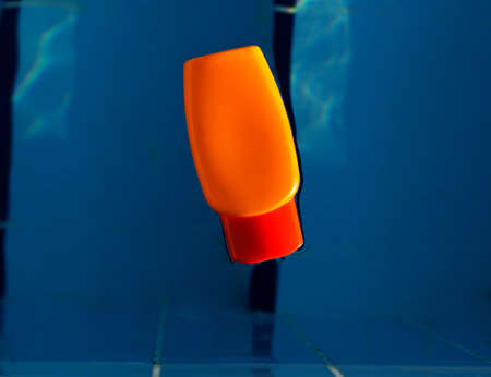 Orange jar with sunscreen uv protected cream is swimming in swimming pool with blue water, summer conceptの写真素材