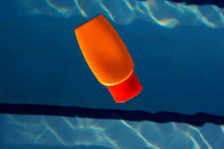 Orange jar with sunscreen uv protected cream is swimming in swimming pool with blue water, summer conceptの写真素材
