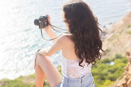 Portrait of tourist happy smiling girl making photos of the nature and sea views by old camera on the peak of mountain over sea backgroundの写真素材