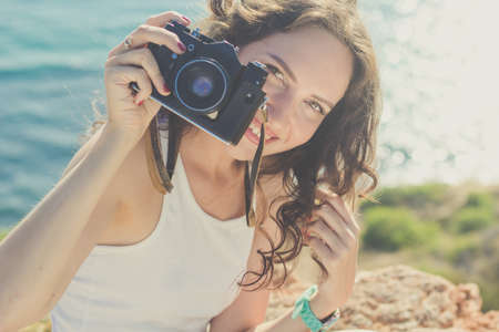 Tourist smiling slim girl making photo by old camera on the peak of mountain over sea background