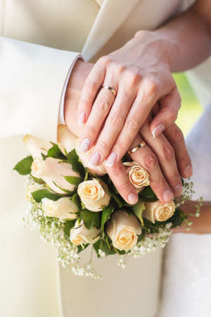 Bride and groom's hands with wedding rings on the bouquet with white rosesの写真素材