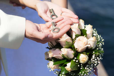 Bride and groom's hands with keys and bouquet with white rosesの写真素材