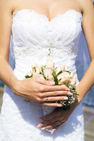Beautiful bride in a white dress in summer time over sea background with a bouquet of roses in handsの写真素材