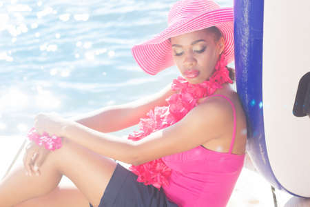 Young south african zulu woman is wearing pink hat and hawaiian flowers is sitting near the seaの写真素材